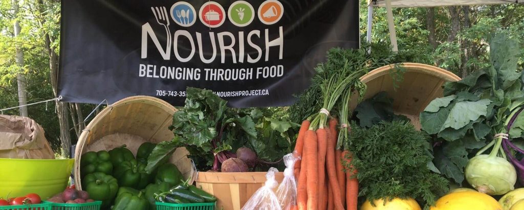 a wide variety of fresh, local vegetables, displayed beneath the Nourish banner