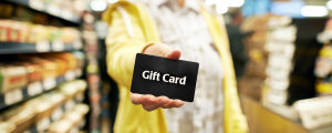 a woman's hand holds out a gift card near the checkout at a grocery store