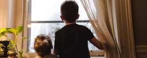 two young children look expectantly out a snowy window