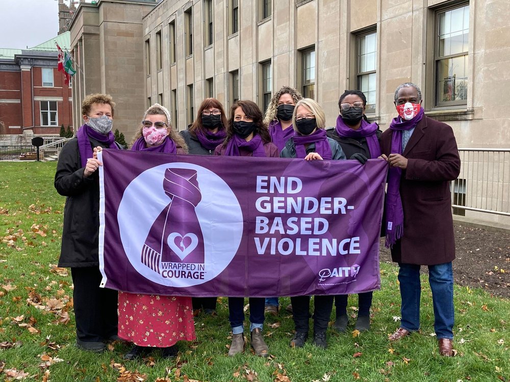 a group of people gather outside Peterborough City Hall, holding a purple "End Gender-Based Violence" flag