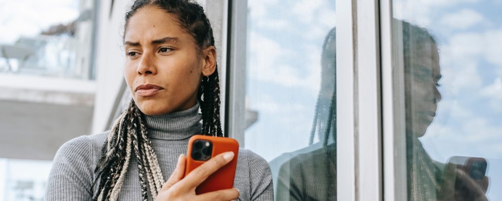 a woman with long braided hair and a serious expression holds a cell phone